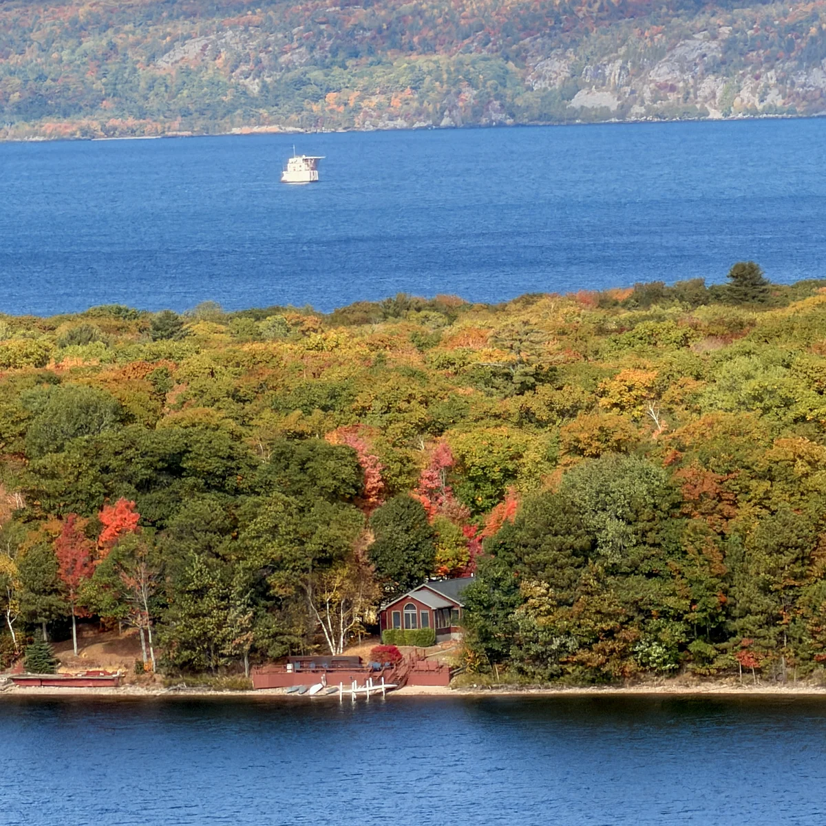 Lakefront home among fall trees with foreground water and a distant freighter